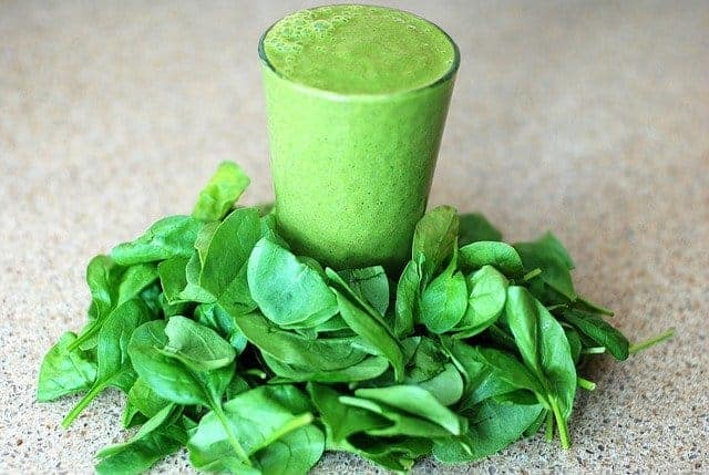 Um copo com um smoothie verde, folhas de espinafre por todo o lado