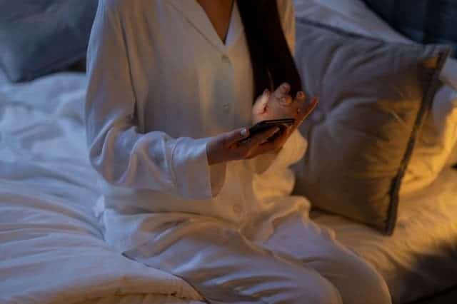 mulher de pijama com o smartphone na mão senta-se na cama