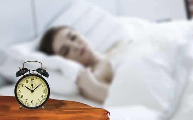  uma mulher dorme com um despertador ao lado da cama.