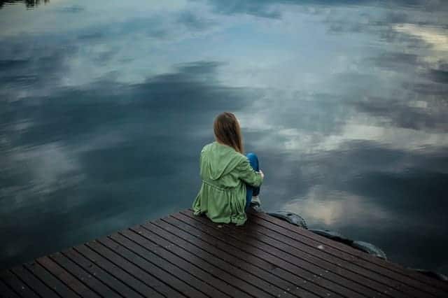  uma mulher senta-se à beira de um cais e olha para dentro de água