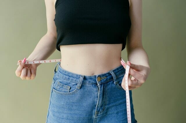  uma mulher mede a sua cintura com um centímetro