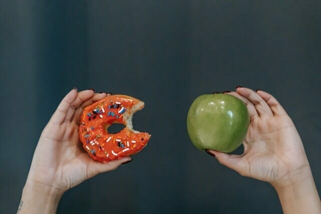  duas mãos, uma segurando uma maçã, a outra um donut