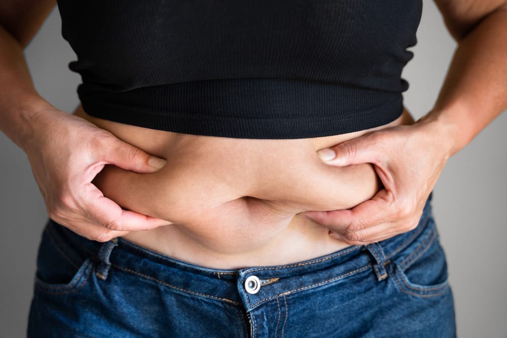 uma mulher segura a barriga e vê a sua gordura corporal aumentar